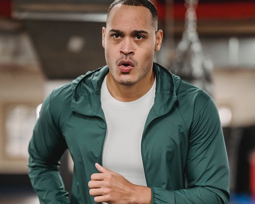 Man running in gym wearing green jacket.