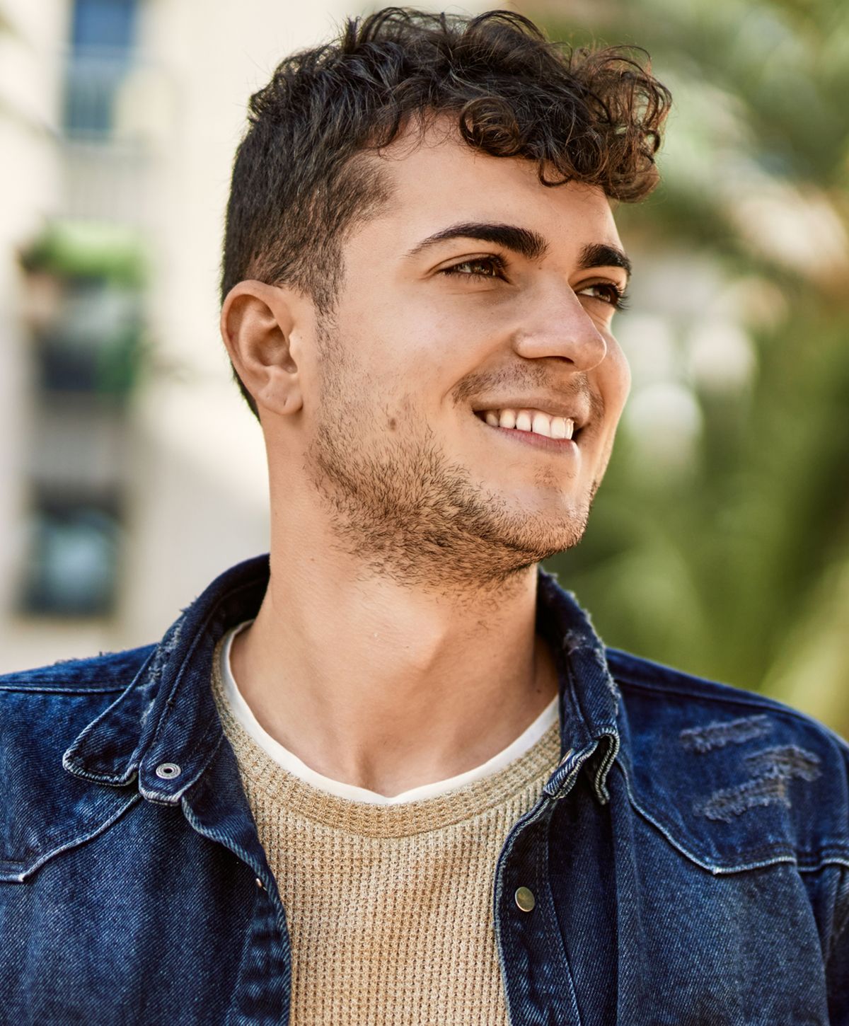 Smiling man in denim jacket outdoors.