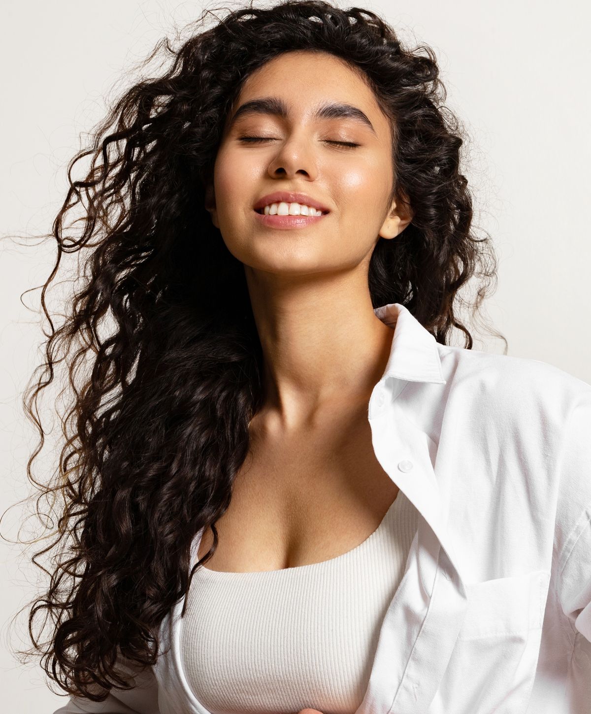 Smiling woman with curly hair wearing white shirt.