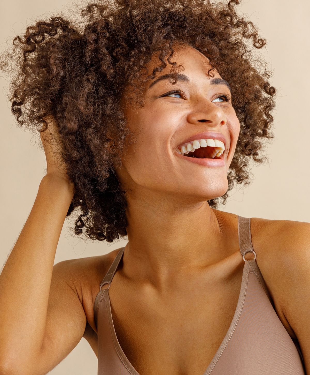 Smiling woman with curly hair against beige background.