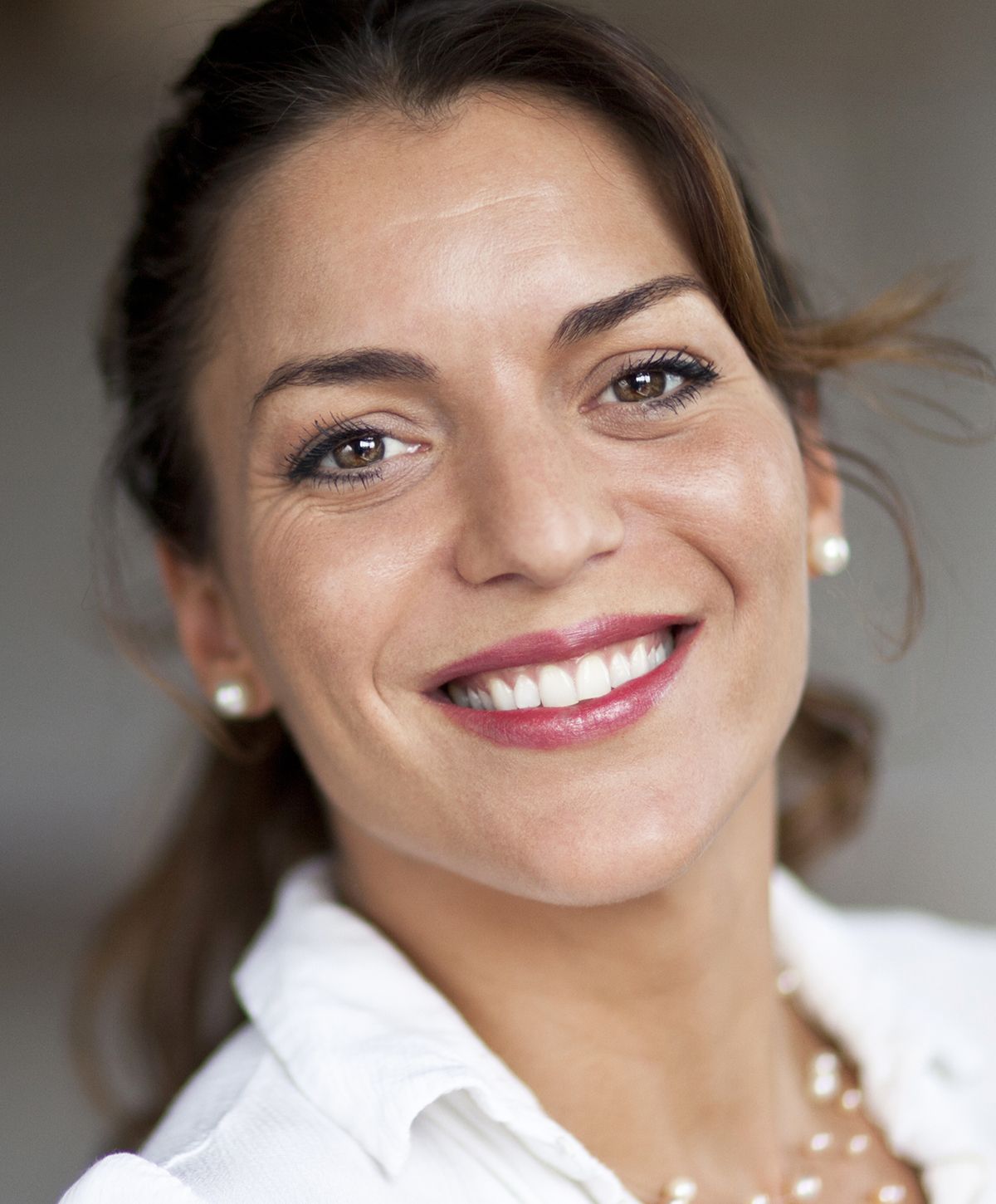 Smiling woman with brown eyes and pearl earrings.
