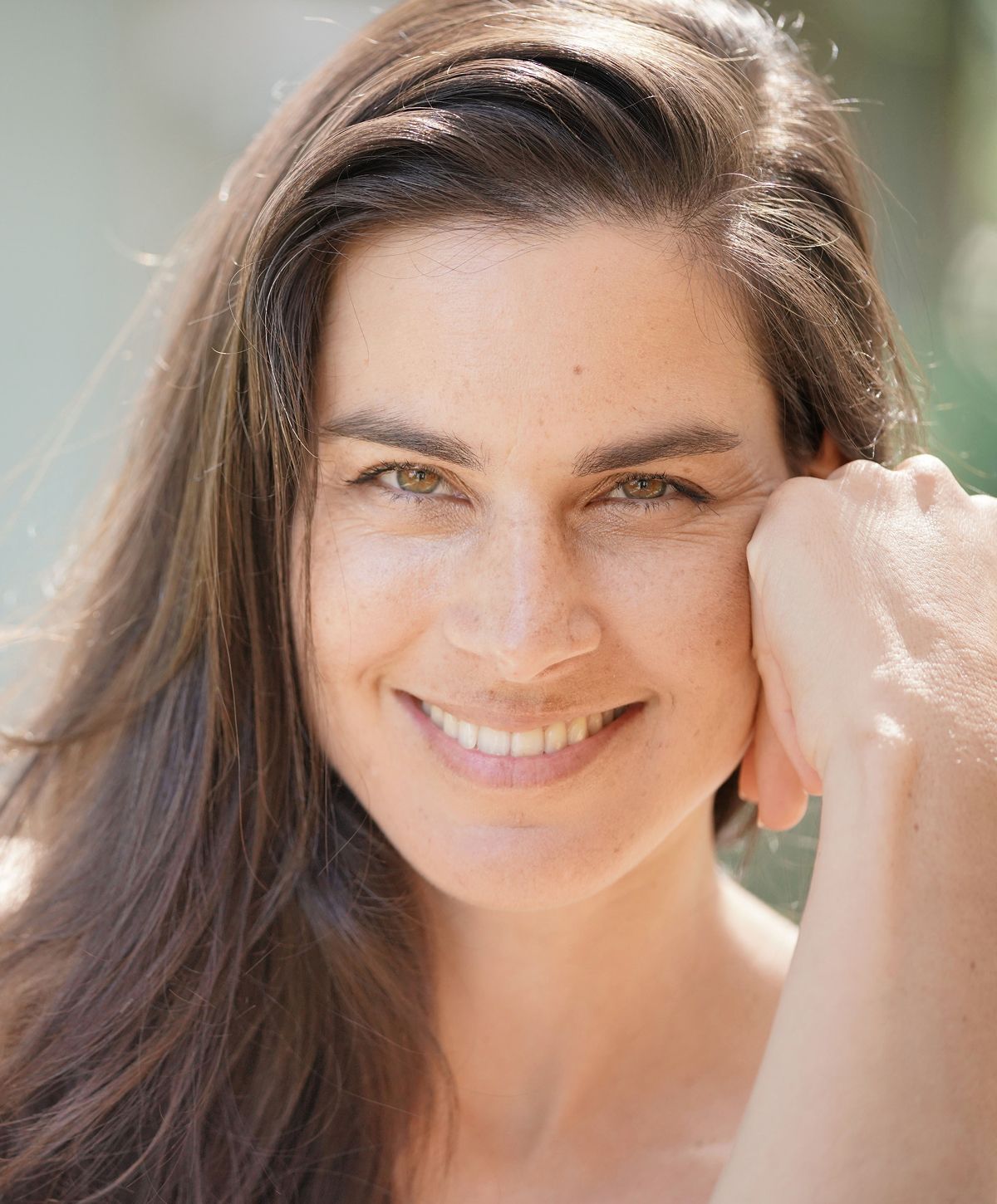 Smiling woman with long dark hair outdoors.