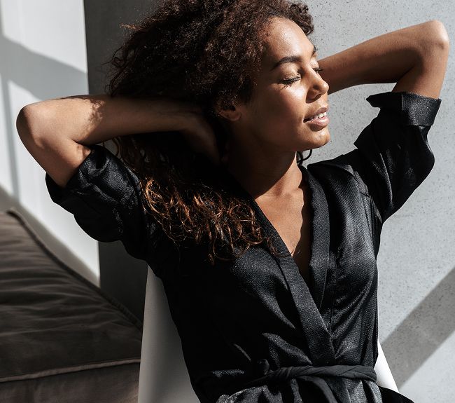 Woman in black dress seated, enjoying sunlight.