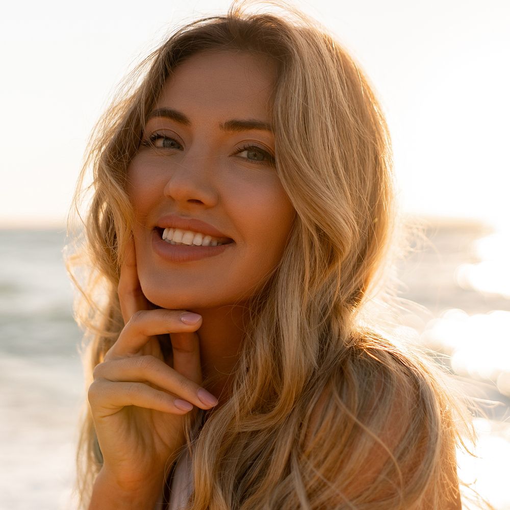 Smiling woman by the beach at sunset.