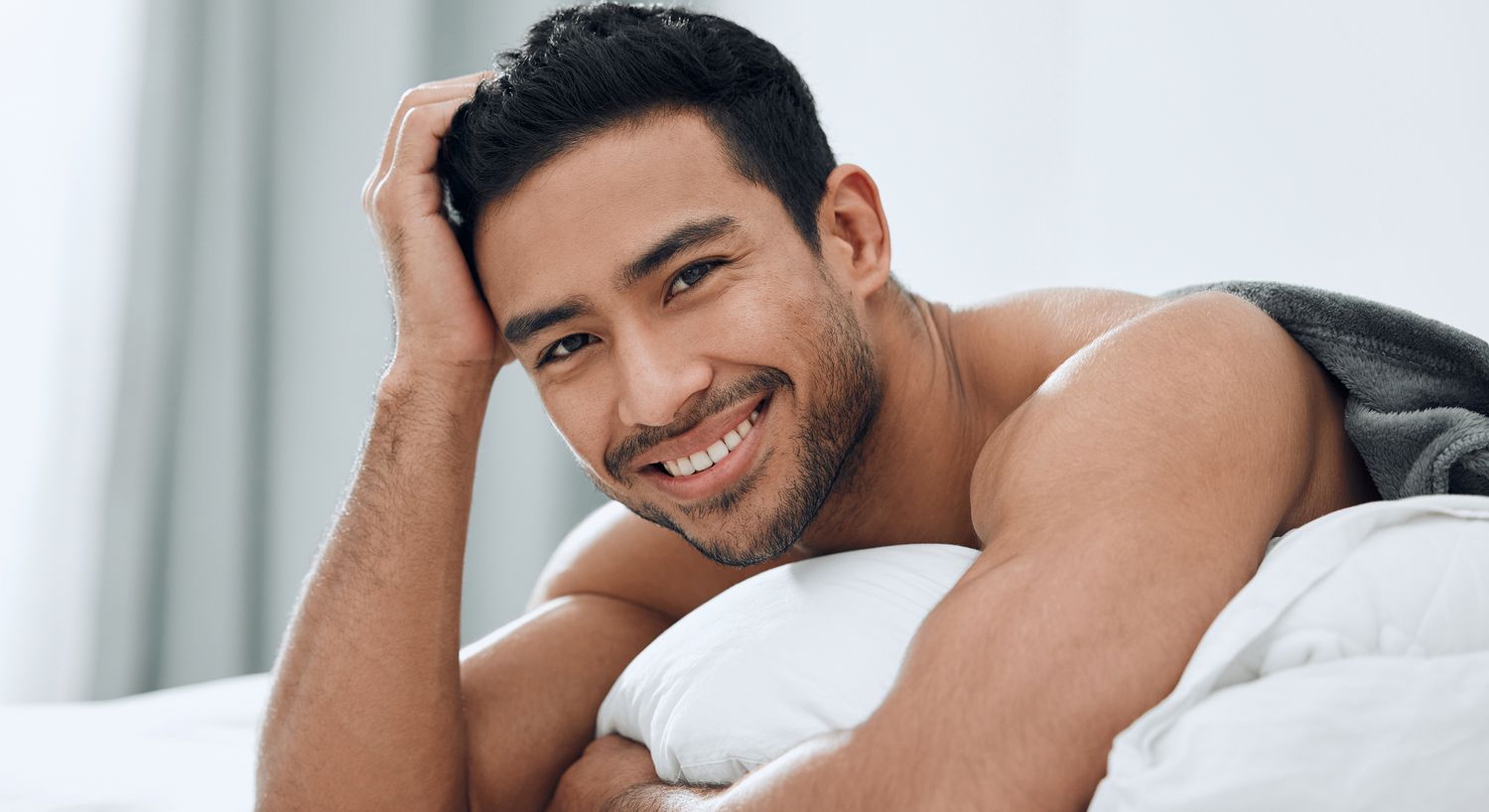Smiling man resting on white pillows.