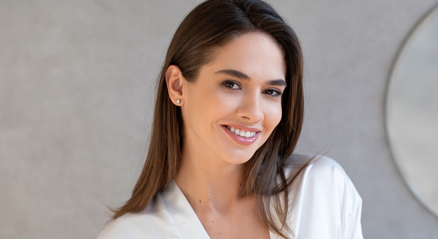 Smiling woman in white robe, neutral background.