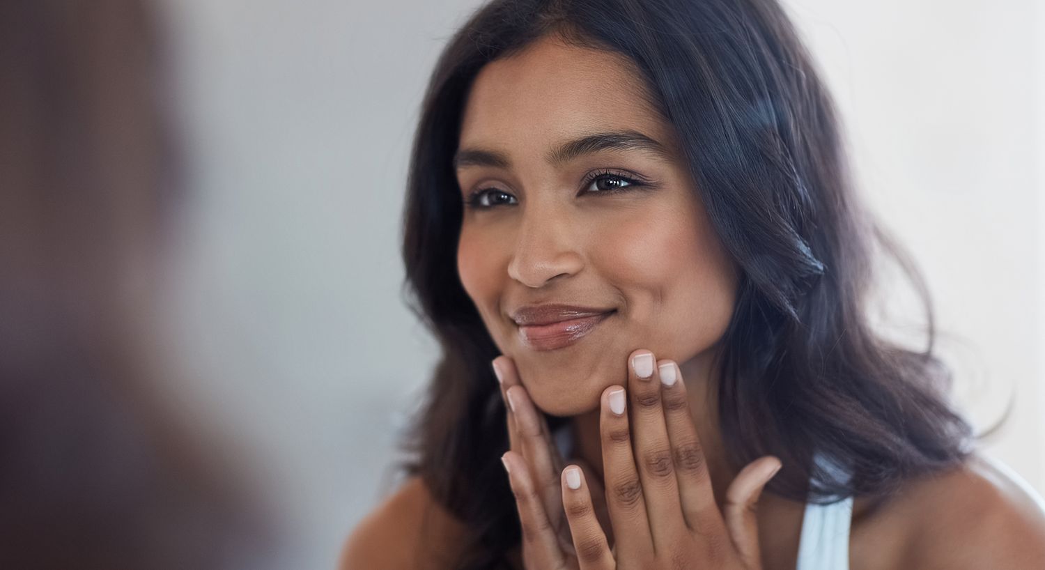 Smiling woman touching her face in mirror.